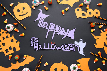 Inscription Happy Halloween with candies and paper decorations on black background