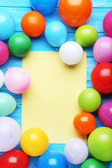 Colorful balloons with sheet of blank paper on wooden table