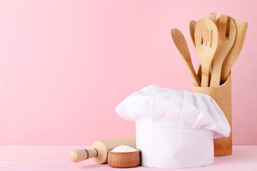 Chef hat with cooking cutlery and flour on pink background
