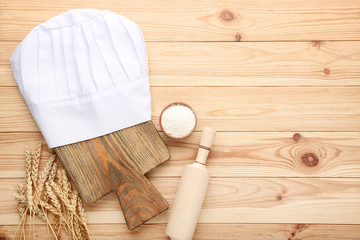 Chef hat with cutting board, rolling pin and wheat ears on brown wooden table
