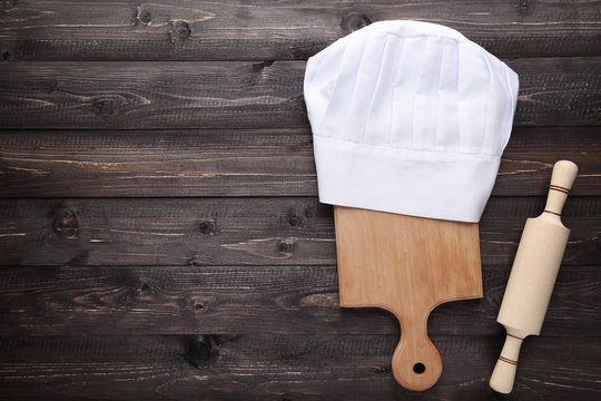 Chef hat with cutting board and rolling pin on wooden table