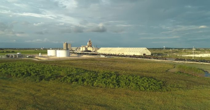Aerial low level orbit left, panning right to large factory, trainyard and green landscape.  It's is just before sunset and the area has the golden hour look.