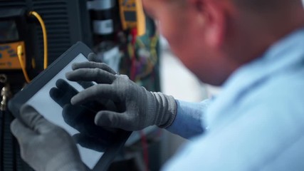 Male HVAC technician uses an ipad tablet while working and fixing an air conditioning unit outside.