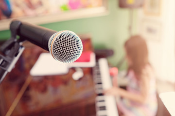 microphone with blurred girl playing piano background, homeschooling music education