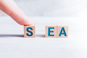 The Word SEA Formed By Wooden Blocks And Arranged By A Male Finger On A White Table