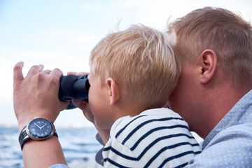 Close up portrait of boy and man sit at the deck and looks through binoculars
