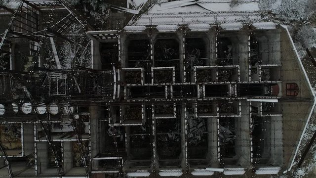 Aerial senital drone scene of destroyed building, old burned hotel in snowy day. Detail Metal structure of construction and top view of rooms distribution. Camera ascends to general view.