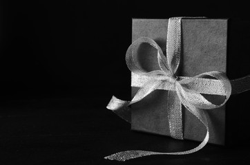 Black gift box with silver ribbon bow on black background