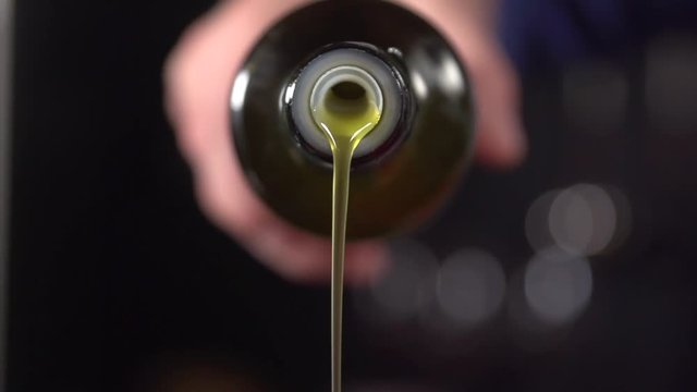 Slow motion shot of extra virgin olive oil being poured over food