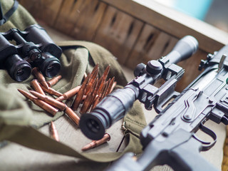 Obraz premium Sniper rifle, binoculars and ammo laying on a wooden floor.