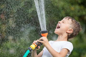 Happy little boy pouring water from a hose.