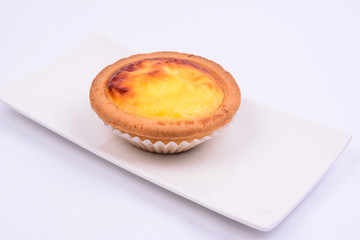 A whole cheese tart in a white ceramic plate isolated on white background.