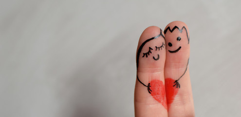 Fingers as happy couple in love with painted smiley faces holding red heart and smiling on light...