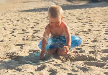 Blonde boy playing with sand on sunny hot beach