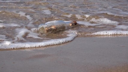 Message in bottle rolling on the sand, vacation on beach