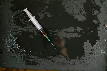 Syringe with a dark liquid on a dark wet background.