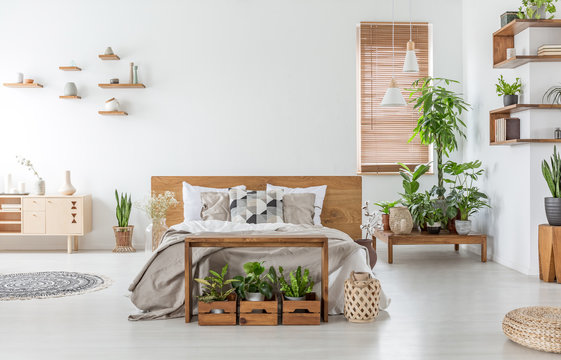 Bed With Wooden Headboard In White Spacious Bedroom Interior With Cupboard And Plants. Real Photo