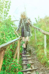 A woman with an umbrella in a raincoat and rubber boots is walking heavily along a self-made ladder.