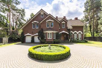 Front view of a driveway with a round garden and big, english style house in the background. Real...