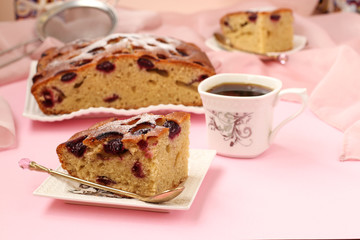 Pie with cherries is located on a pink background on a plate. On the table a cup of coffee 