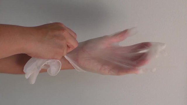 Female putting clear plastic glove on left hand.