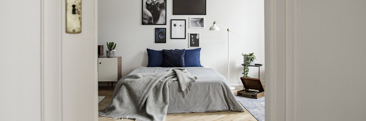 Real photo of a modern bedroom interior with a double bed and art collection. View through a door
