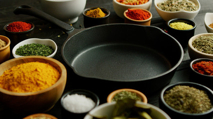 From above view of bowls with colorful spices and black pan placed in middle