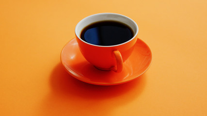 From above view of cup with hot black coffee on orange background