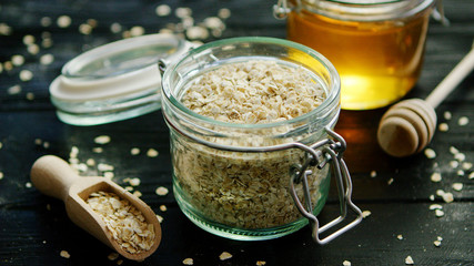 From above view of oat in glass jar placed on wooden background with bowl of honey near