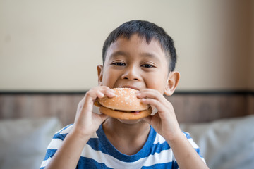 happy Asian boy eating hamburger in restaurant
