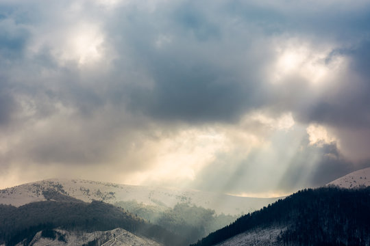 overcast sky with light beams over the ridge. dramatic winter scenery in mountains with snowy tops