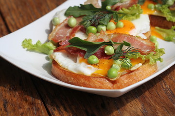 Bruschetta with rucola, chrispy bacon, green pea and poached egg served on white plate
