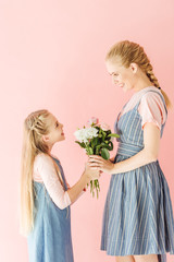 happy young mother and daughter holding beautiful bouquet and looking at each other isolated on pink