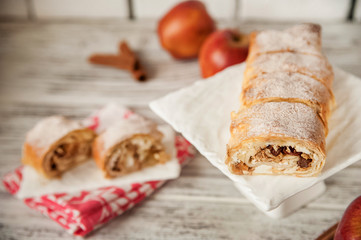 Apple strudel on a white square plate close-up and cut. Apple pie and red apples, cinnamon. Bright textural background with space for text