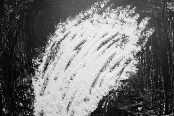 White flour in middle on black background texture photo, lines drawn with finger on flour, abstract. monochrome, black and white. top view.