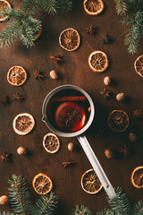 top view of hot spiced wine in saucepan with dried orange slices on wooden background with pine branches