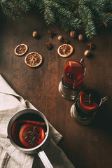 Obraz na płótnie Canvas mulled wine in saucepan and glass cups on wooden background with dried orange slices and spices