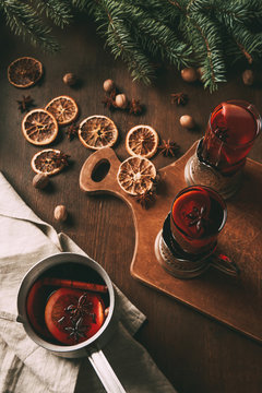 hot mulled wine in saucepan and glass cups on cutting board with dried orange slices and spices