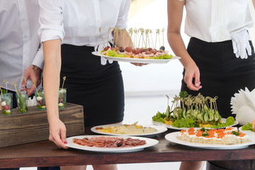 Two waiters serves banquet table in white marquee outdoor. Hands closeup
