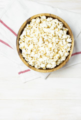 Brown wooden bowl with delicious traditional popcorn on a light wooden background. Top view of a light meal background.