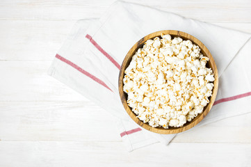 Brown wooden bowl with delicious traditional popcorn on a light wooden background. Top view of a light meal background.