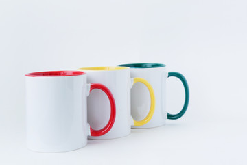Three white mugs, with a green, yellow, green handle on a light background. 