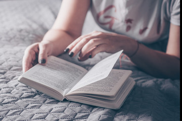 Girl reading a book on grey cozy bed. Home Concepts. Place for text