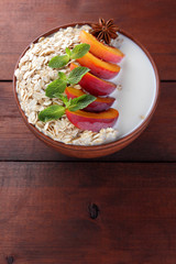 Oatmeal with fruits and green mint. Oat flakes with milk on wooden background. Healthy food. Breakfast for vegan. Dry oats with peaches, anise and milk. Copy space
