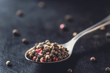 close-up view of spoon with dried aromatic peppercorns on black