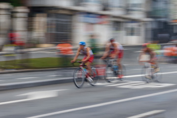 Fototapeta na wymiar Blurred silhouettes of bicyclists on a blurred city background