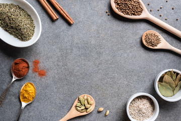 various aromatic dried seasonings in bowls and spoons on grey background