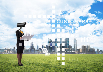 Camera headed woman standing on green grass against modern cityscape