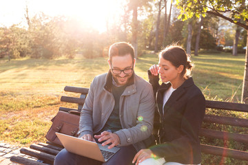 Businessman and businesswoman using laptop while sitting on bench at park