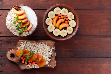 Oatmeal with fruits and green mint. Oat flakes with milk and dried apricots on wooden background. Healthy food for vegans. Dry oats with peaches, anise and berries of mountain ash. Copy space